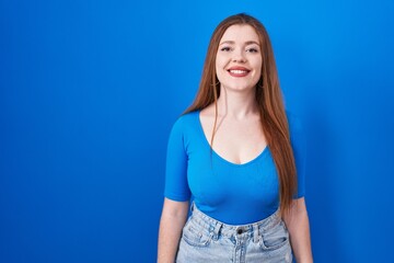 Poster - Redhead woman standing over blue background with a happy and cool smile on face. lucky person.