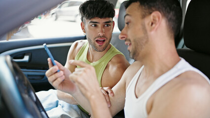 Poster - Two men couple using smartphone sitting on car at street