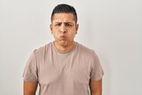 Fototapeta  - Hispanic young man standing over white background puffing cheeks with funny face. mouth inflated with air, crazy expression.