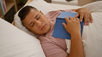 Canvas Print - Handsome young latin man, cozily sleeping away the morning, book comfortably resting on his chest, lying relaxed in the comfort of his bedroom bed at home