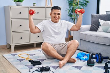 Sticker - Young latin man smiling confident using dumbbells training at home