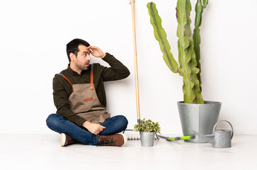 Poster - Gardener man sitting on the floor at indoors with surprise expression while looking side