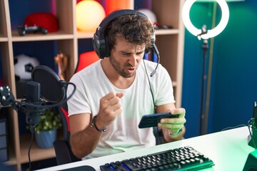 Canvas Print - Young hispanic man streamer playing video game using smartphone at music studio