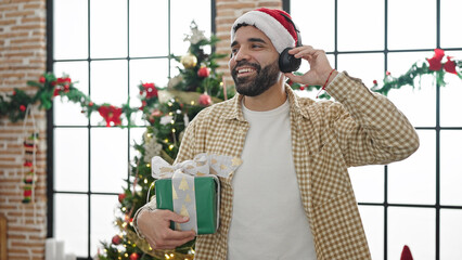 Sticker - Young hispanic man listening to music holding christmas gift at home