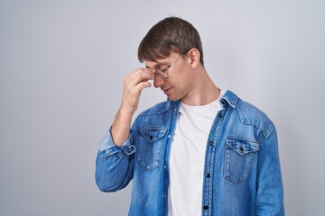 Wall Mural - Caucasian blond man standing wearing glasses tired rubbing nose and eyes feeling fatigue and headache. stress and frustration concept.