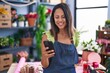Young hispanic woman florist smiling confident using smartphone at florist store