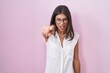 Brunette young woman standing over pink background wearing glasses pointing displeased and frustrated to the camera, angry and furious with you