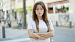 Young beautiful hispanic woman standing with serious expression with arms crossed gesture at street