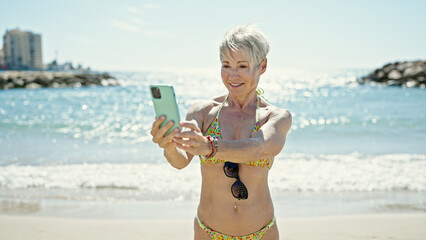 Wall Mural - Middle age blonde woman tourist wearing bikini using smartphone at the beach
