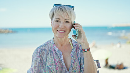Wall Mural - Middle age blonde woman tourist smiling confident talking on smartphone at the beach