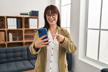 Canvas Print - Young brunette woman working at the office with smartphone smiling happy pointing with hand and finger