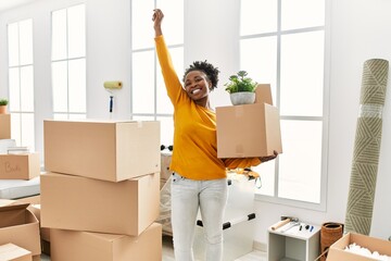 Canvas Print - African american woman holding package standing with winner expression at new home