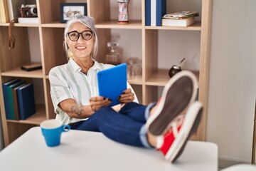 Sticker - Middle age grey-haired woman drinking coffee and using touchpad at home