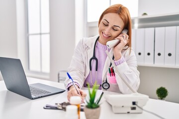 Poster - Young caucasian woman doctor talking on telephone writing medical report at clinic