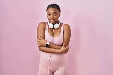 Canvas Print - African american woman with braids wearing sportswear and headphones shaking and freezing for winter cold with sad and shock expression on face