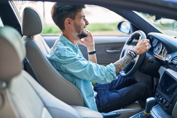 Poster - Young hispanic man talking on smartphone sitting on car at street