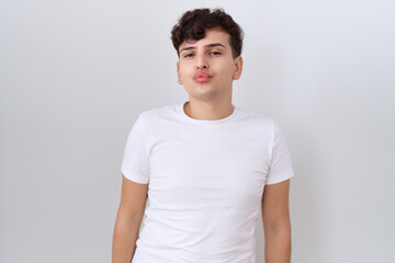 Wall Mural - Young non binary man wearing casual white t shirt looking at the camera blowing a kiss on air being lovely and sexy. love expression.