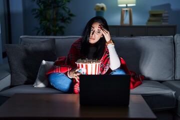 Sticker - Hispanic woman eating popcorn watching a movie on the sofa worried and stressed about a problem with hand on forehead, nervous and anxious for crisis