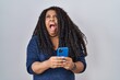 © Krakenimages.com - Plus size hispanic woman using smartphone typing message angry and mad screaming frustrated and furious, shouting with anger looking up.