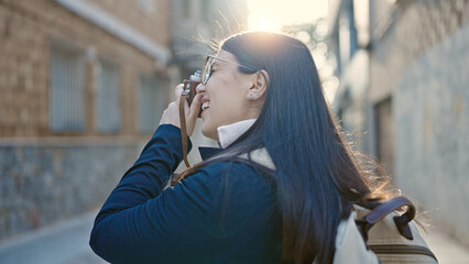 Poster - Young hispanic woman tourist wearing backpack taking pictures with camera at street