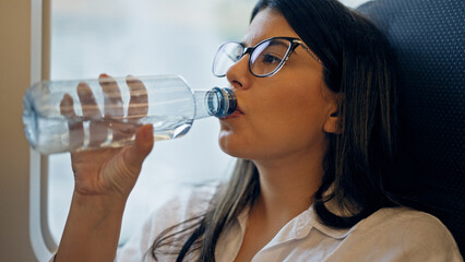 Sticker - Young beautiful hispanic woman drinking water from plastic bottle inside train wagon