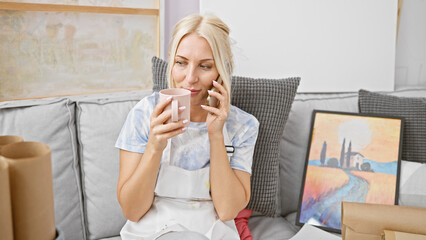 Poster - Engrossed young blonde art student chats vivaciously on smartphone, savoring coffee amid a creative classroom bustle at the university studio