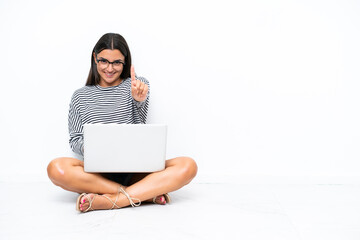 Wall Mural - Young caucasian woman with a laptop sitting on the floor showing and lifting a finger