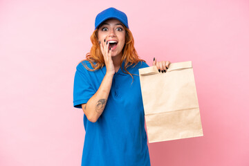 Wall Mural - Young caucasian woman taking a bag of takeaway food isolated on pink background with surprise and shocked facial expression