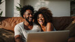 Young multiracial couple laughing looking at laptop sitting on sofa at home, happy diverse husband and wife using online services on internet, technology lifestyle concept