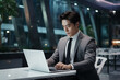 © boval - Successful male businessman of Asian appearance in a business suit works at a laptop. Generative AI