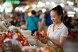 Cheerful young Vietnamese woman buying fruits at local market to make apple pie