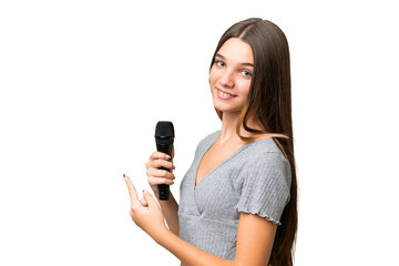 Canvas Print - Teenager singer girl picking up a microphone over isolated background pointing back