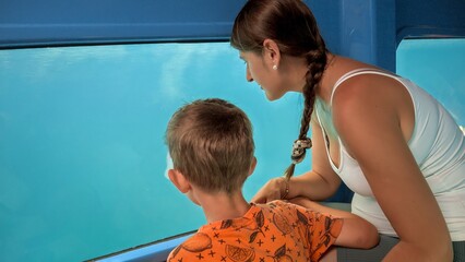 Wall Mural - Happy boy with young mother having a tourist trip on submarine and looking on fishes through window. Holiday, summer vacation and tourism