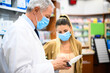 © Minerva Studio - Pharmacist wearing a face mask and a woman in a pharmacy