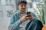 Fototapeta  - young man with mobile phone sitting on the sofa at home