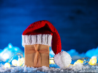 Canvas Print - A Christmas gift in a Santa hat on a snow table. Blue background, copy space