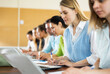 © JackF - Portrait of concentrated womens and mens studying in classroom, listening to teacher and writing in notebook