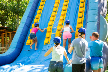 Two active sporty young women having funny competition in climbing on inflatable castle with wooden sticks in summer outdoor amusement park..