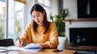 © InputUX - A young woman in a yellow top is concentrated on reviewing documents at a well-lit home workspace, exemplifying remote work.