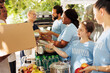 © DC Studio - Friendly girl and volunteers provide food to needy at charity food drive. Voluntary individuals distribute meal boxes and donation packages, including canned goods, to support the poor and homeless.
