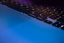 Close-up of laptop keyboard and touchpad in neon lighting