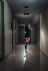 A young scared woman in a panic runs away along a dark corridor.