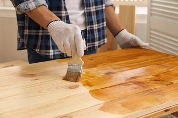 Poster - Man with brush applying wood stain onto wooden surface indoors, closeup