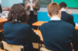 © tsuguliev - Kids in school writing and taking notes, teens pupils behind desks during the lesson listen to teacher lecture, classroom with students and classmates, group of teenagers during test and exam