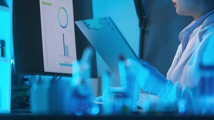 Medical Research Scientist Typing Sophisticated Coding on Her Desktop Computer in a Biological Applied Science Research Laboratory. Lab Engineers in White Coats Conduct Experiments in the Background.