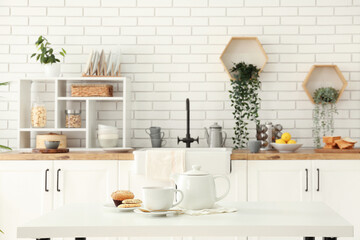 Poster - Interior of light kitchen with teapot, cup and snacks on table