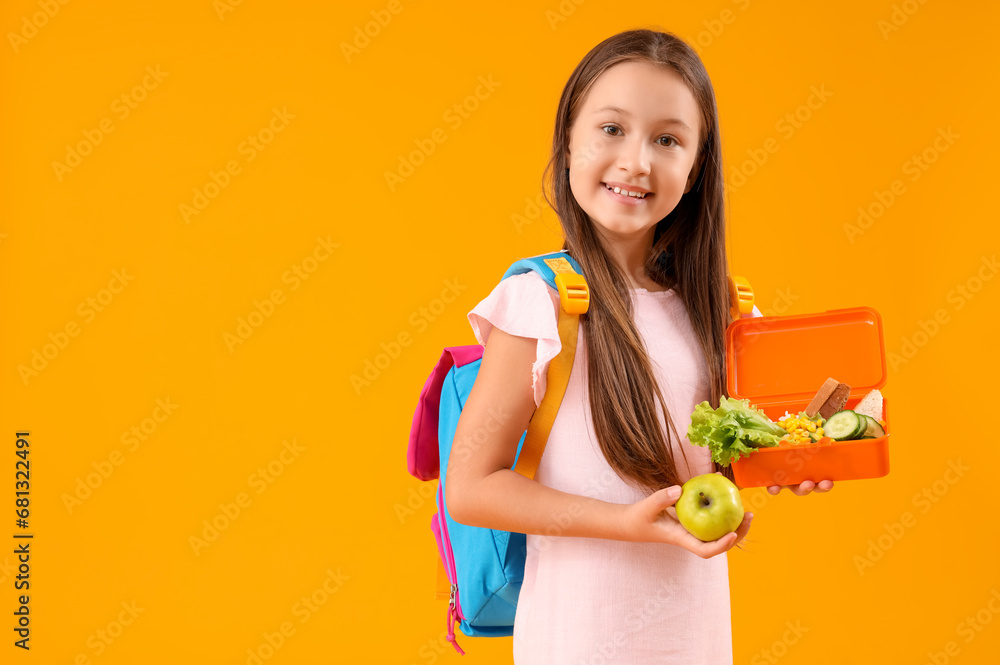 Happy little girl with backpack, lunchbox and apple on yellow background
