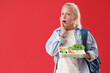 Shocked girl with backpack and lunchbox on red background