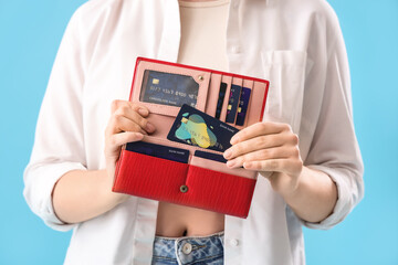 Poster - Young woman with credit card and wallet on blue background, closeup