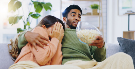 Wall Mural - Fear, jump and couple watching tv on a sofa with popcorn for movie, film or streaming show at home. Omg, television and people hug in living room with cinema snack for scary, horror or spooky series